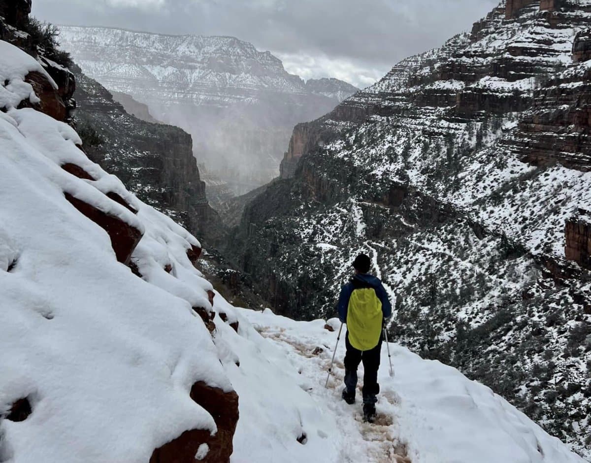 A hiker on a snow covered ledge looking out over the Grand Canyon
